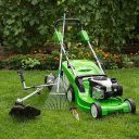 Green lawnmower, weed trimmer, rake and secateurs in the garden